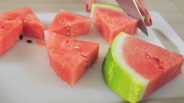 Beyaz kadın olgun karpuz dilimlerini bıçakla kesip kaseye koyuyor. Piknik için çekirdeksiz kırmızı karpuz kesen kız, yemek yiyor. Sağlıklı gıda konsepti, mevsim meyvesi, yaz partisi, atıştırmalıklar..