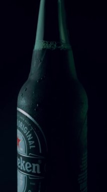 İtalya, Roma - 23. 06 numara. 2021 dikey video. Yeşil Heineken birasının kapağı siyah arka planda dönüyor. Görüntüleri ayır. Alman birası ayna masasında kendi etrafında döner..