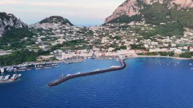 Bereketli yeşillikler ve yükselen uçurumlarla çevrili Capri limanının nefes kesen manzarası güneş batarken ılık bir ışıltı yayıyor ve kayıklar yavaşça suda sallanıyor..