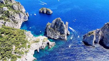 Çarpıcı bir hava perspektifi, canlı mavi denizin manzaralı bir kıyı şeridi boyunca dramatik kaya oluşumlarıyla buluştuğunu gösteriyor. Tekneler suda süzülüyor, huzur veren güzelliği artırıyor..