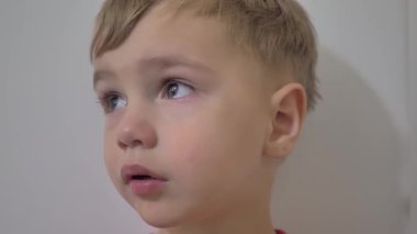 Genç bir çocuk sessizce duruyor, düşüncelere dalmış, büyük gözleri merakı ve merakı yansıtıyor. Kapalı alan ortamları anın sıcaklığını arttırır, gülümsemeleri cezbeder..