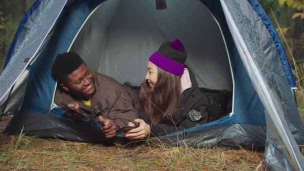Различные путешественники с гаджетами, отдыхающие в палатке лагеря — стоковое видео