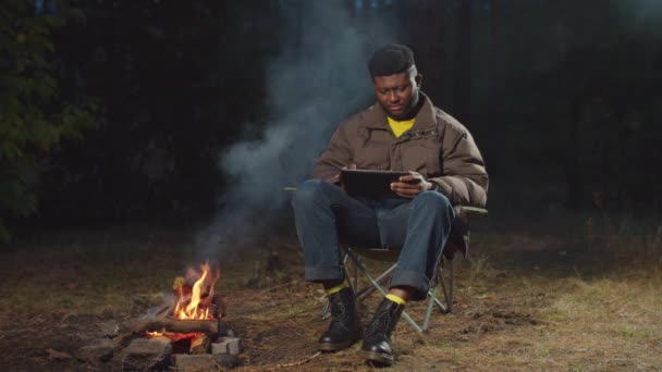 Afrikaanse reiziger werkt op tablet pc door kampvuur — Stockvideo