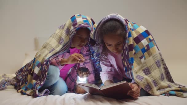 Hermanas de edad elemental leyendo libro bajo manta — Vídeo de stock