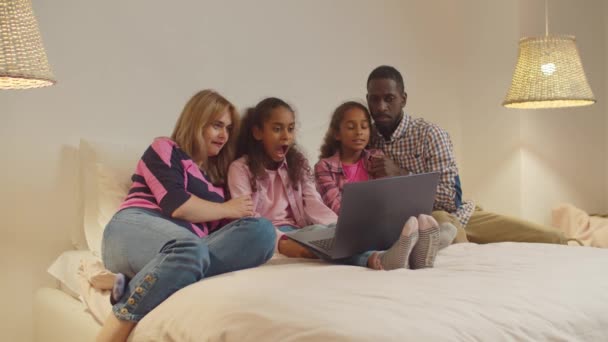 Разнообразные семьи смотрят страшные фильмы онлайн в постели — стоковое видео