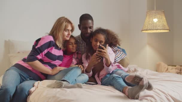 Yatakta selfie çeken kızların olduğu ırklar arası bir aile. — Stok video