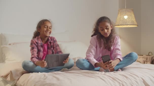 Mädchen im Grundalter mit Gadgets, die auf dem Bett ruhen — Stockvideo