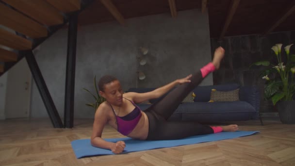 Siyah formda kadın yan yatarak bacak kaldırma egzersizi yapıyor. — Stok video