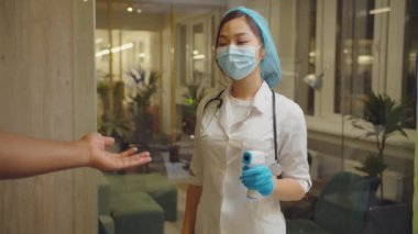 Hasta sıcaklığını ölçen Asyalı kadın doktor.