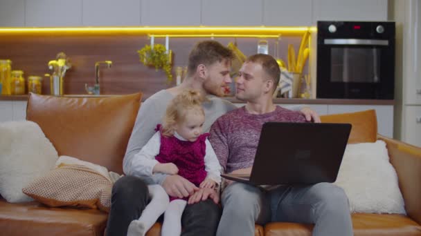 Счастливая гей-семья с маленькой девочкой, отдыхающей на диване — стоковое видео