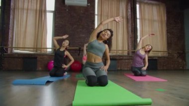 Çeşitli spor formundaki kadınlar yan eğik egzersizler yapıyor.