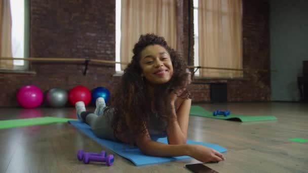 Smiling black female lying on fitness mat indoors — Stock Video