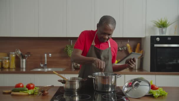 Starší muž v kuchyni připravuje jídlo pomocí tabletu ks — Stock video