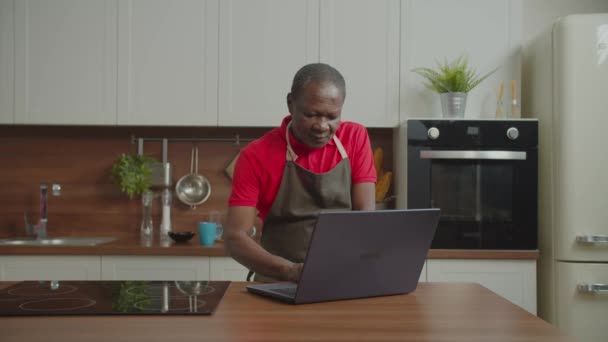 Emerytowany afrykański mężczyzna networking na laptopie w kuchni — Wideo stockowe