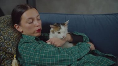 Kanepede mırıldayan kediyi kucaklayan rahat, güzel bir kadın.