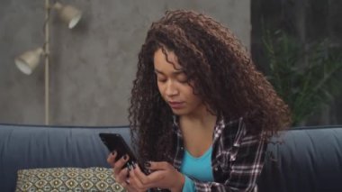 Üzgün siyahi kadın internette cep telefonuyla mesajlaşıyor.