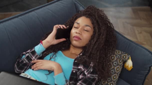 Красивая черная женщина говорит на смартфоне на диване — стоковое видео
