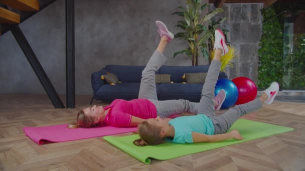 Mamá y su hija haciendo ejercicio de piernas bajas en interiores — Vídeo de stock