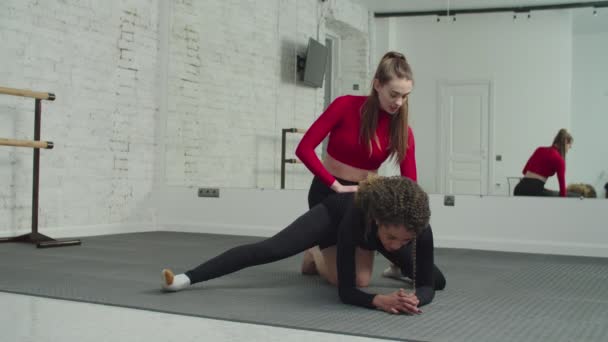 Treinador pessoal ajudando a mulher no treino de alongamento no ginásio — Vídeo de Stock