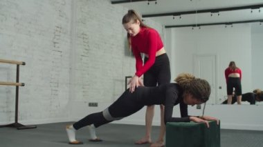 Formda bir kadın antrenörle kalas egzersizi yapıyor.