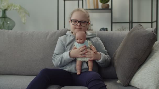 Joyeux enfant avec le syndrome du duvet étreignant poupée sur le canapé — Video