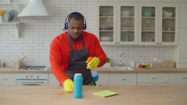 Hombre africano positivo en la limpieza de auriculares en la cocina — Vídeos de Stock