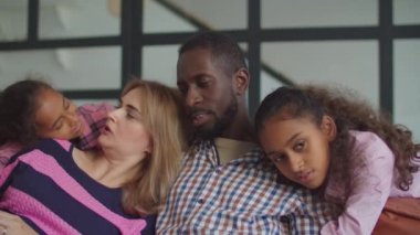 Çocukların kanepede kaynaştığı çeşitli bir aile.