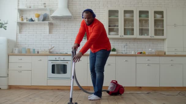 Zwarte man in koptelefoon stofzuigen in de huiselijke keuken — Stockvideo