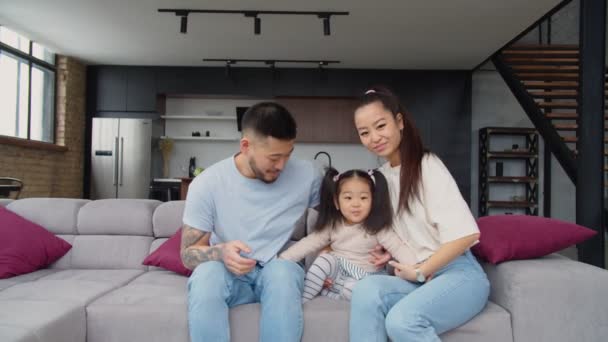 Feliz asiático padres y bebé chica agitando mano en sofá — Vídeos de Stock