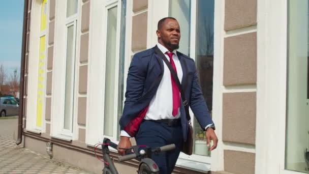 Zwarte mannelijke ondernemer met elektrische scooter langs straat — Stockvideo