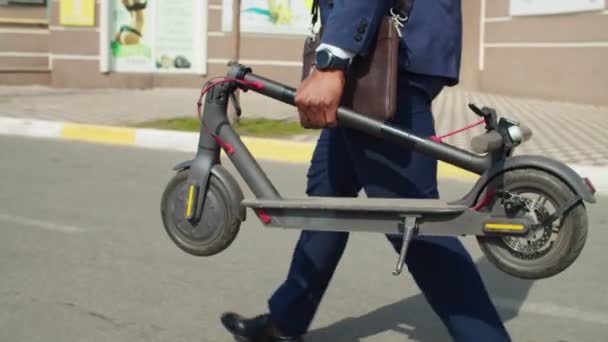 Empresário carregando scooter elétrico dobrado ao longo da rua — Vídeo de Stock