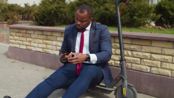 Бизнесмен, сидящий на электронном скутере и разговаривающий на смартфоне — стоковое видео