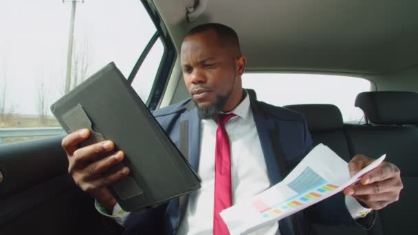 Negro hombre de negocios que trabaja con la tableta PC en el asiento trasero del coche — Vídeos de Stock