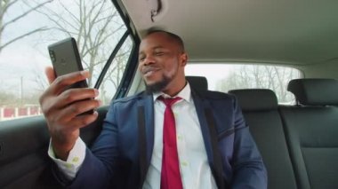 Afrikalı erkek girişimci araç içinde cep telefonuyla video konferansı yapıyor