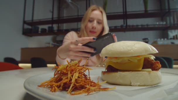 Mujer bloguera de comida tomando fotos de sabrosa hamburguesa en el teléfono — Vídeo de stock