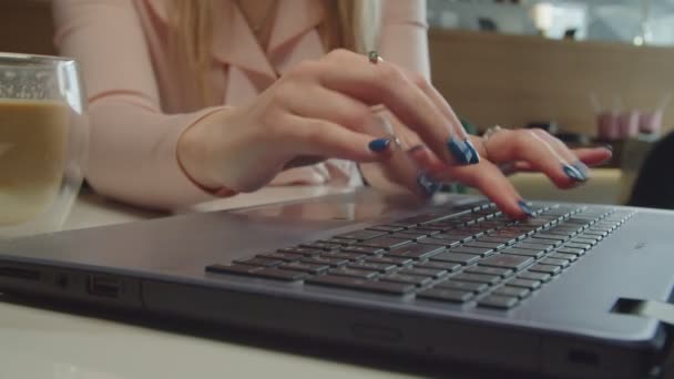 Primer plano de manos femeninas escribiendo en el teclado del ordenador portátil en la cafetería — Vídeo de stock