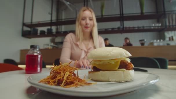 Mujer encantadora tomando sabrosa hamburguesa fresca en las manos en la cafetería — Vídeo de stock