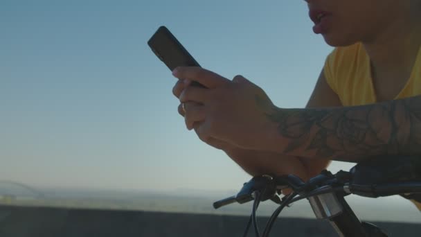 Close-up of female cyclist chatting online on smartphone at sunrise — Stock Video