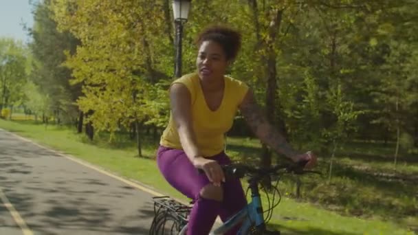 Alegre muito africano mulher ciclista andando de bicicleta através do parque — Vídeo de Stock