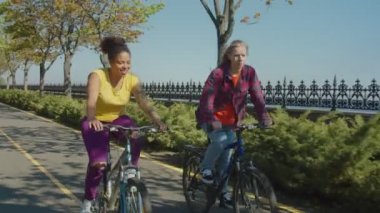 Park sokağında bisiklete binen aktif çok ırklı kadın arkadaşlarının portresi