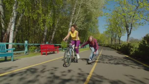 Милая черная женщина на велосипеде и буксировка подруги на скейтборде — стоковое видео