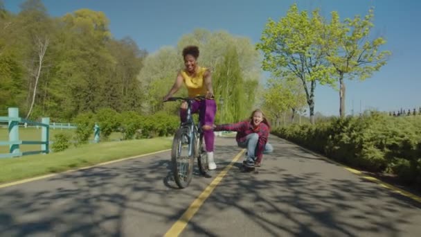 Веселые многорасовые женщины наслаждаются отдыхом, катанием на велосипеде и скейтборде на свежем воздухе — стоковое видео