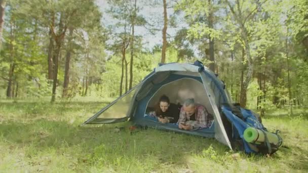 Positieve backpacker koppel op kampeerreis met behulp van mobiele telefoons in de tent — Stockvideo