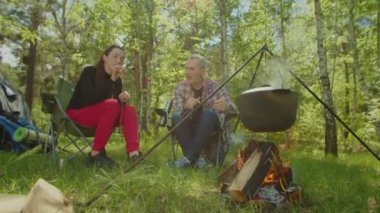 Hiker couple camping in forest, eating roasted marshmallows