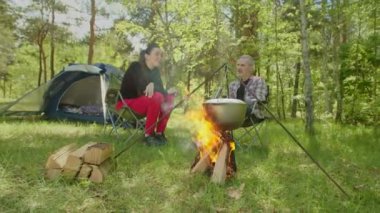 Cheerful backpackers talking and relaxing near campfire during hike