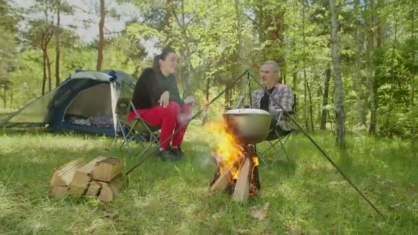 Cheerful backpackers talking and relaxing near campfire during hike — 图库视频影像