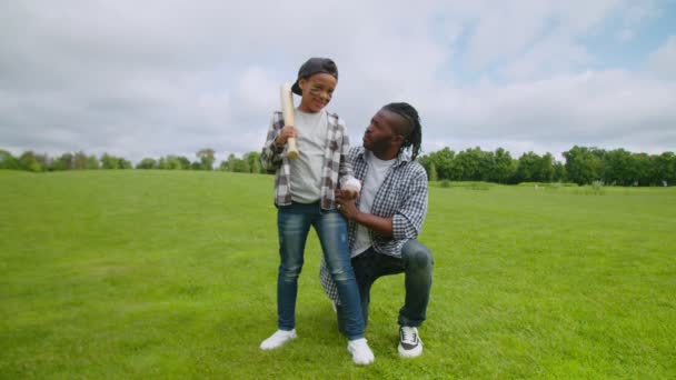 Догляд за американським батьком вчить маленького хлопчика грати в бейсбол на полі — стокове відео
