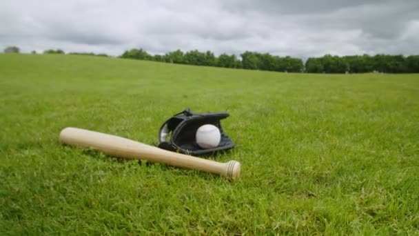 Бейсбольна рукавичка, м'яч і дерев'яна кажана лежать на зеленому полі — стокове відео