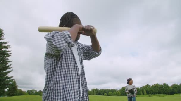 Närbild av afrikansk pappa med basebollträ slagsmål söner tonhöjd på planen — Stockvideo