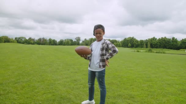 Улыбающийся черный школьник с американским футбольным мячом на поле — стоковое видео
